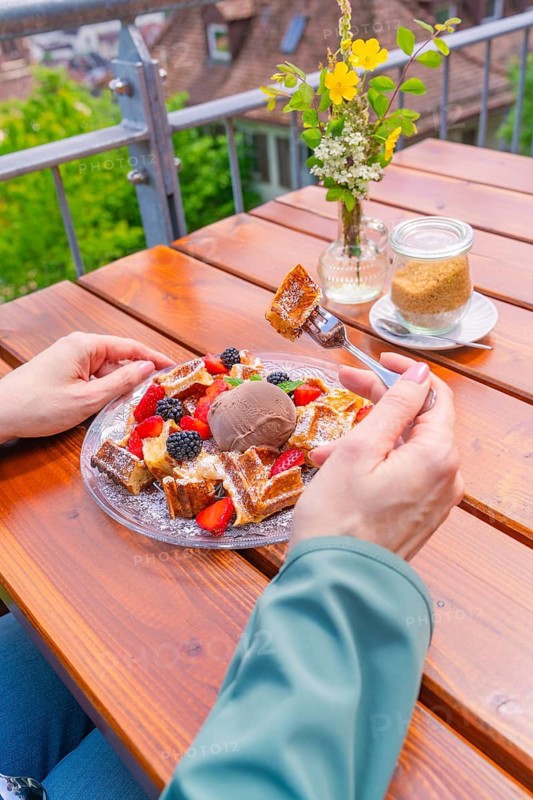 Person enjoying waffles with berries and ice cream on a balcony with a view, Cafehäusle Calw, Black Forest, Germany