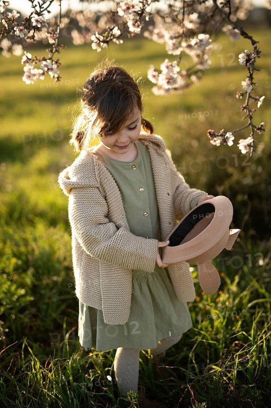 A gentle portrait of a young girl in a cozy sweater and dress, delighting in the surroundings of blooming almond trees during a sunny spring day