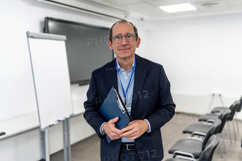Experienced businessman and professor in a suit stands confidently with clipboard, gazing at camera in a modern office ready to lead a corporate presentation or educational seminar