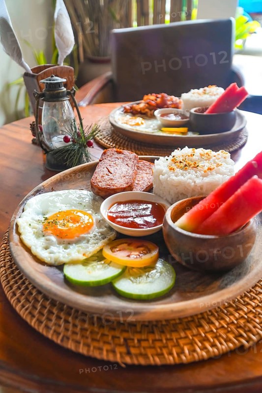 Delicious filipino breakfast featuring rice, fried egg, luncheon meat, watermelon, tomato, cucumber, and sauce, served on a wooden plate in siargao island