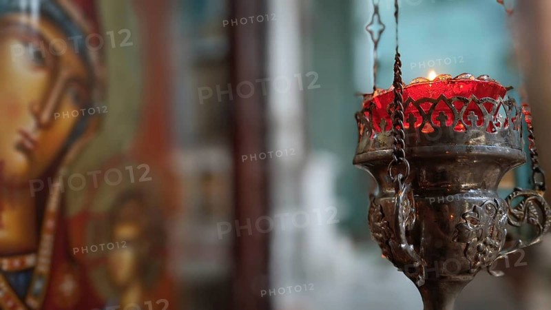 A burning candle in front of an iconic painting in an atmospheric Orthodox church, Georgia