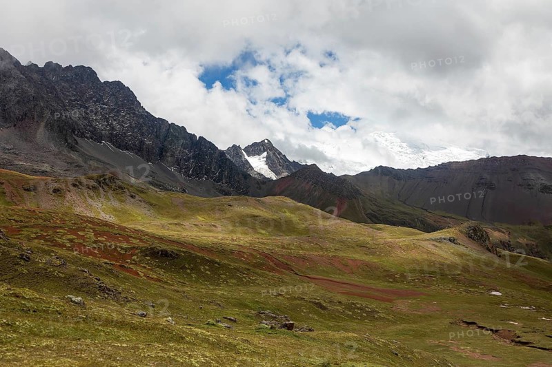 This vivid image captures the stunning natural beauty of Peru's Andean mountains, showcasing lush green fields and rugged peaks partially covered with snow