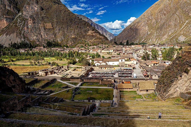 Extensive view of a village in the valley surrounded by high mountains under blue skies, the town of Ollantaytambo in the Andes of Peru