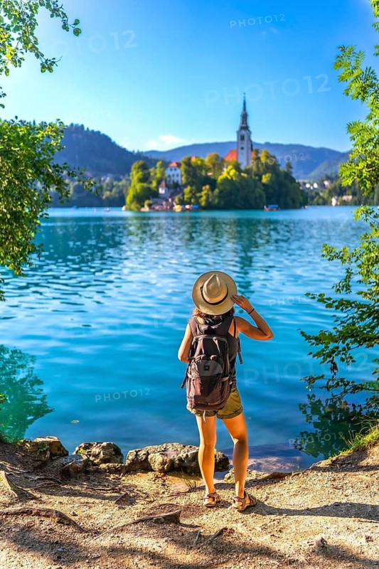Female tourist with backpack and hat admiring the assumption of mary pilgrimage church on lake bled island, a famous travel destination in the julian alps