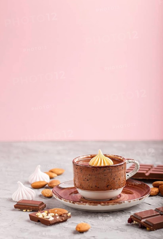 Cup of hot chocolate and pieces of milk chocolate with almonds on a gray and pink background. side view, close up, selective focus, copy space