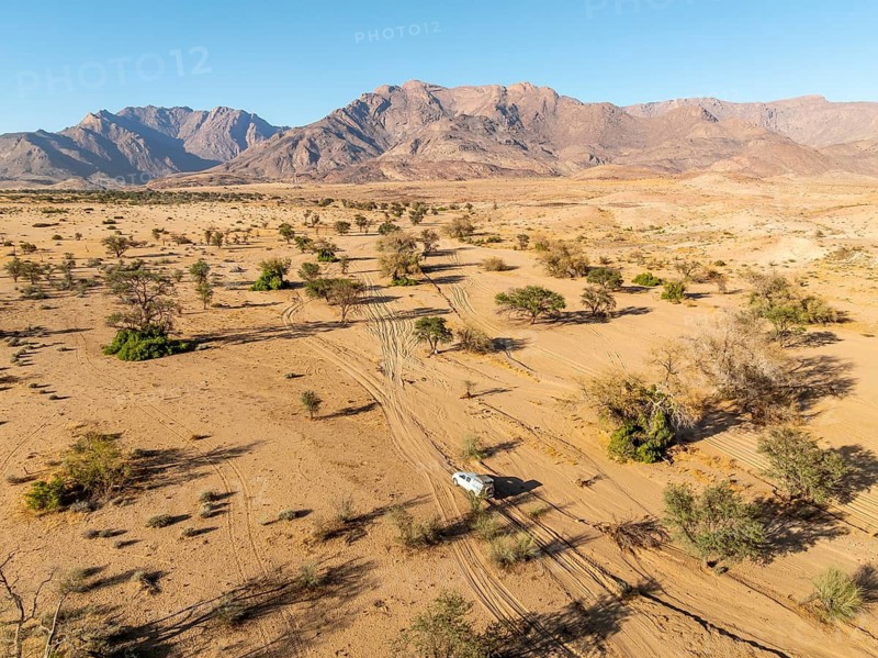 Aerial view of off-road car driving in dry riverbed and desert landscape on the Ugab River, behind Brandberg, Erongo, Damaraland, Namibia