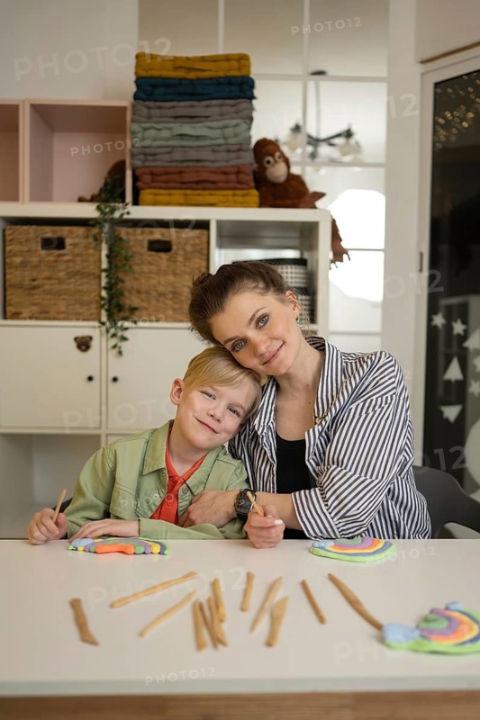 Teacher and student sitting at a table, making crafts with colored clay and sticks, creating a warm and creative environment