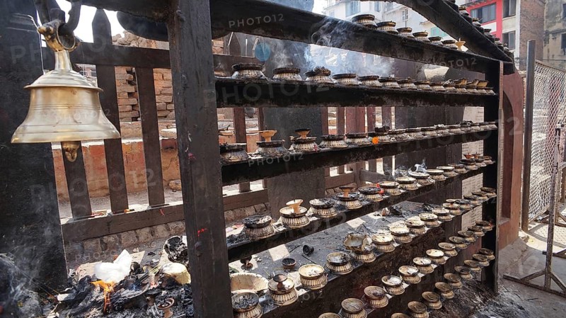 Solemn religious site with burning candles in front of a temple and a small bell tower, Kathmandu, Nepal