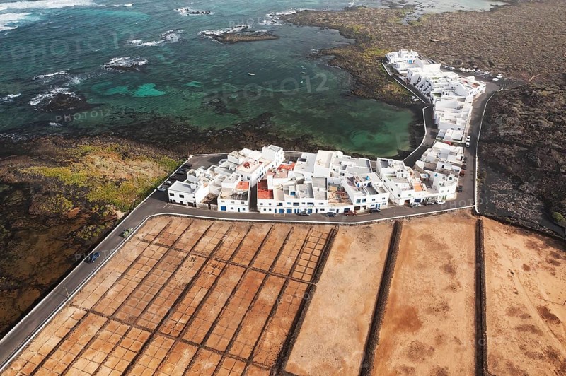 Aerial shot of the vibrant Salares de Orzola in Lanzarote, showcasing the salt pans adjacent to a quaint coastal town with turquoise waters near residential area with white houses