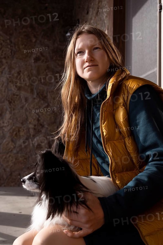 A person in a yellow vest sits with their purebred papillon dog on their lap, capturing a serene moment in the sunlight. The scene conveys warmth and companionship