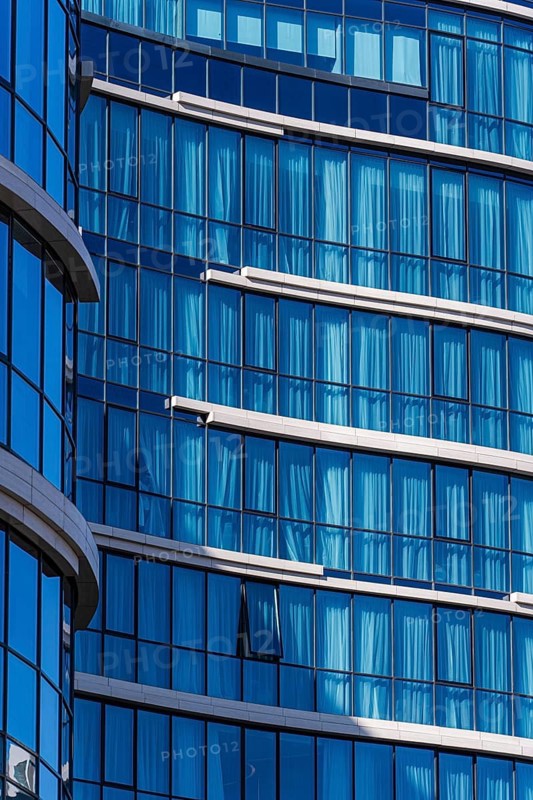 Close-up view of a contemporary building showcasing a reflective blue glass facade, accented by concrete and metal details, symbolizing modern architectural design