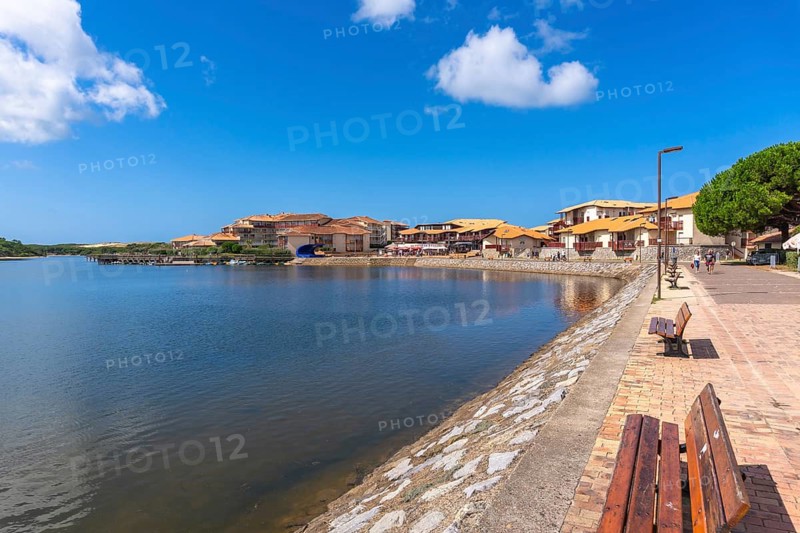 Vieux boucau les bains village on the landes coast in france, with residential buildings and shops lining the serene marine lake and a brick promenade reflecting holiday atmosphere
