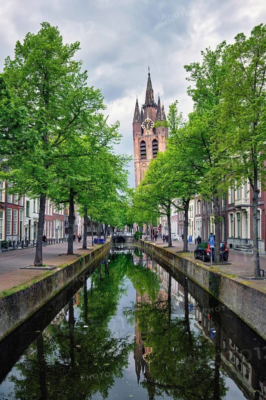 Delt canal with old houses bicycles and cars parked along and Oude Kerk Old church tower. Delft, Netherlands