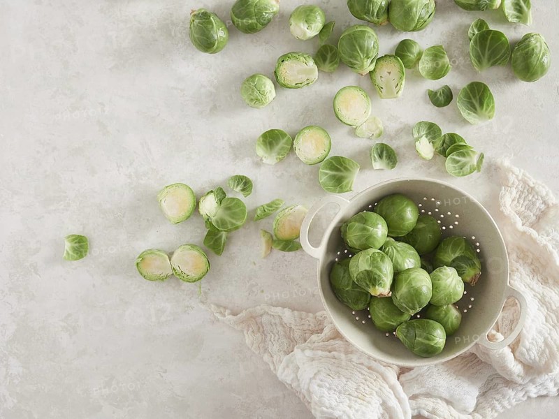 A bunch of fresh green raw brussels sprouts on the countertop, others in a colander. Top view