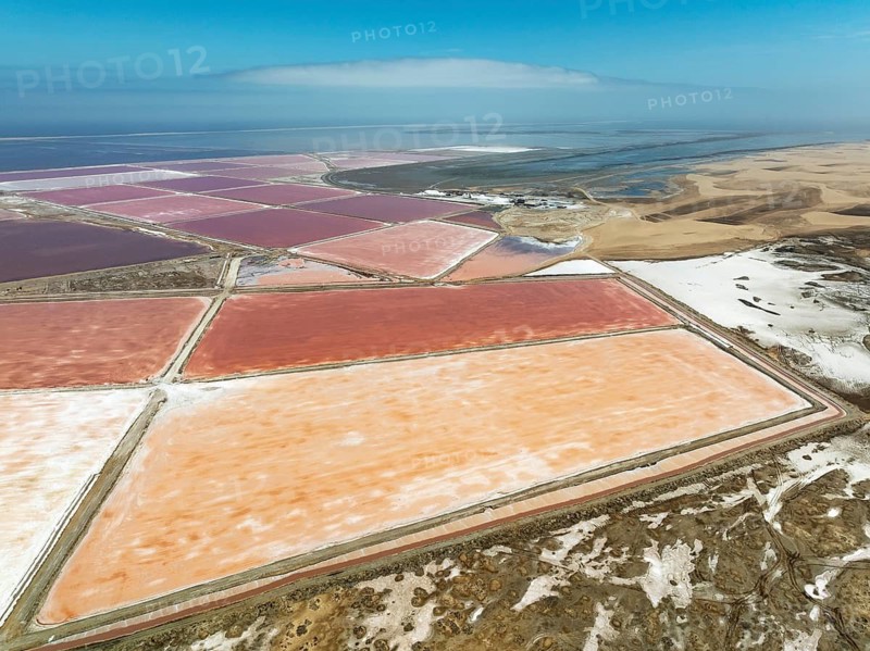 Saline ponds at the salt works of Walvis Bay Salt adjoining the Walvis Bay lagoon and the dunes of the Namib Desert. Aerial view. Drone shot. Walvis Bay, Namibia