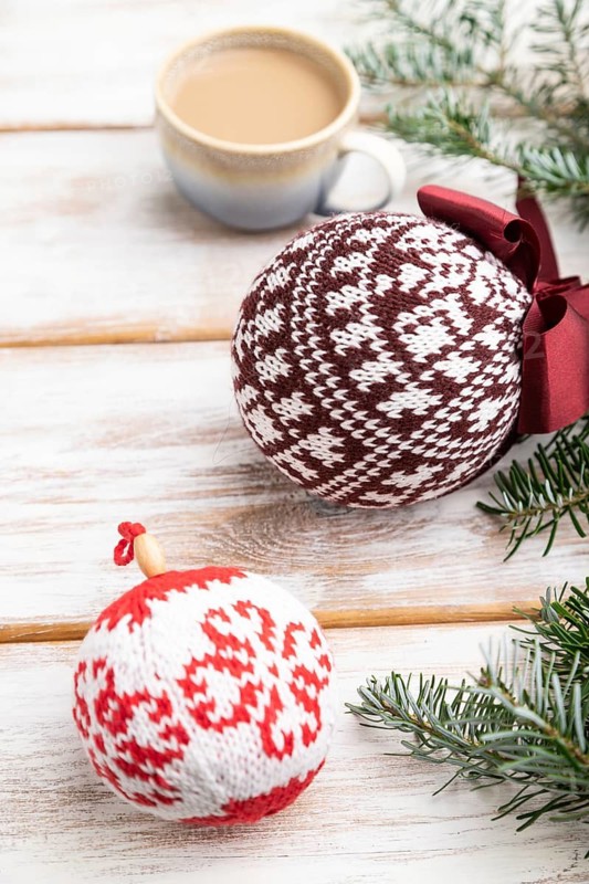 Christmas or New Year composition. Decorations, knitted balls, fir and spruce branches, cup of coffee, on a white wooden background. Side view, close up, selective focus