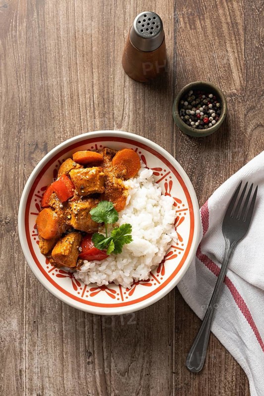 Top view of a traditional Hungarian pork goulash with tender pieces of meat and sliced carrots, served alongside fluffy white rice in a decorative bowl, perfect for a hearty meal