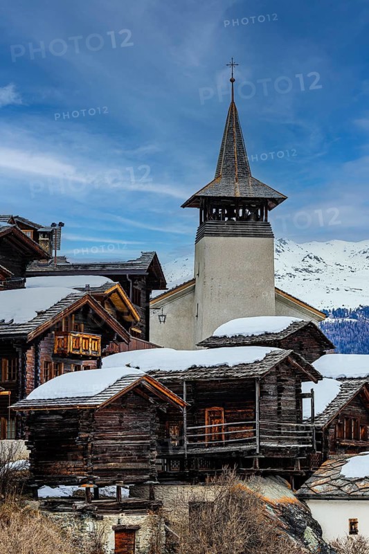 Old wooden houses with snow-covered roofs and the Saint Theodule church in the historic village centre, Grimentz, Val d'Anniviers, Valais Alps, Canton Valais, Switzerland