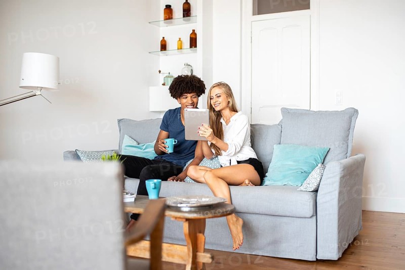 A couple sits comfortably on a stylish gray sofa, enjoying each other's company while browsing a tablet. Their bright and modern living room creates a warm and inviting atmosphere