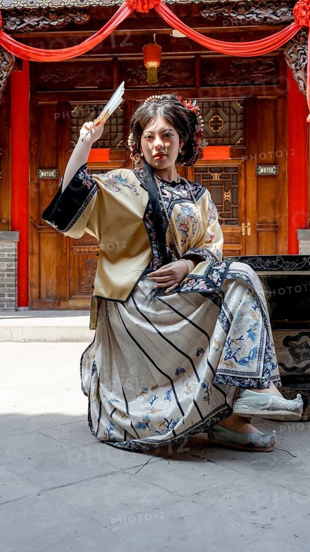 Woman dressed in traditional Qing dynasty clothing, holding a fan, and looking at the camera. Photographed in Pingyao, China, showcasing rich cultural heritage