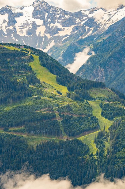 Landscape photograph of mountains with green pastures, snowy peaks and wooded hills, Zillertal, Austria, Germany