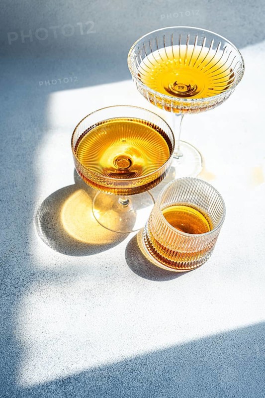 A still life of Georgian amber wine elegantly presented in three distinct glass styles. The light captures the rich, golden hues of the wine, creating a warm, inviting atmosphere
