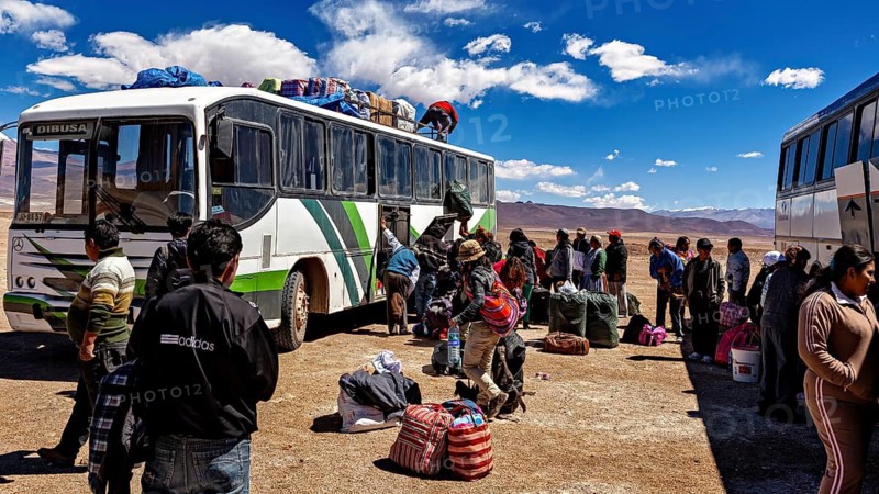 Travelers load luggage on a bus in a dry desert landscape in bright sunshine, bus station in the town of Ollagüe in the Chilean Atacama Desert