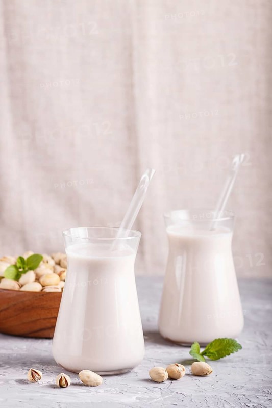 Organic non dairy pistachio milk in glass and wooden plate with pistachio nuts on a gray concrete background. Vegan healthy food concept, close up, side view, copy space