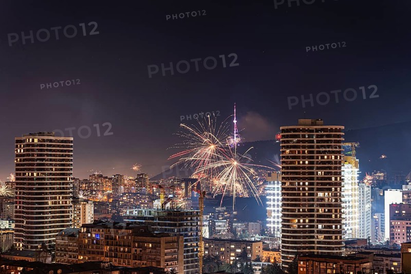 A vibrant display of fireworks illuminates the night sky over Tbilisi's downtown. Skyscrapers and city lights enhance the festive atmosphere, capturing the city's lively spirit