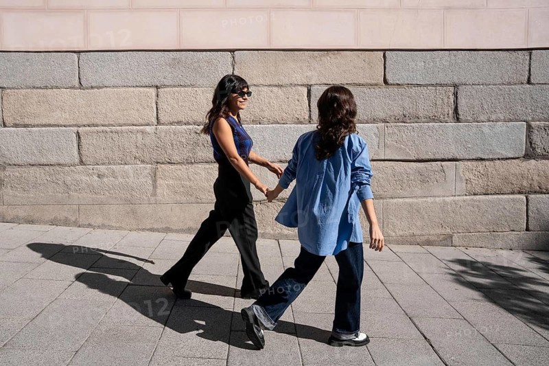 A joyful multiethnic lesbian couple enjoys a sunny day outdoors while holding hands. This image captures love, pride, and diversity in an LGBTQIA+ context