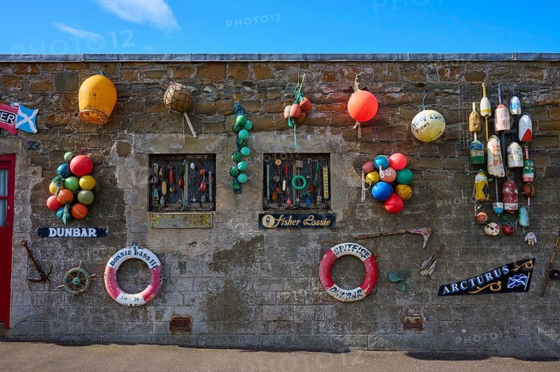A stone wall decorated with colorful buoys and maritime elements against a blue sky, Dunbar, East Lothian, Scotland, United Kingdom, Great Britain
