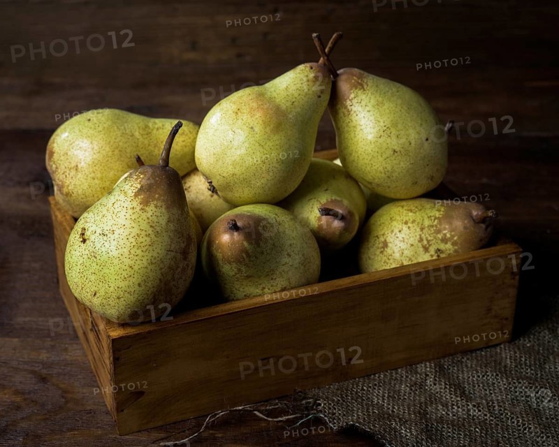 A collection of ripe pears arranged in a rustic wooden box, set on a dark wooden table. The scene gives a cozy and earthy feel, perfect for autumn or harvest themes