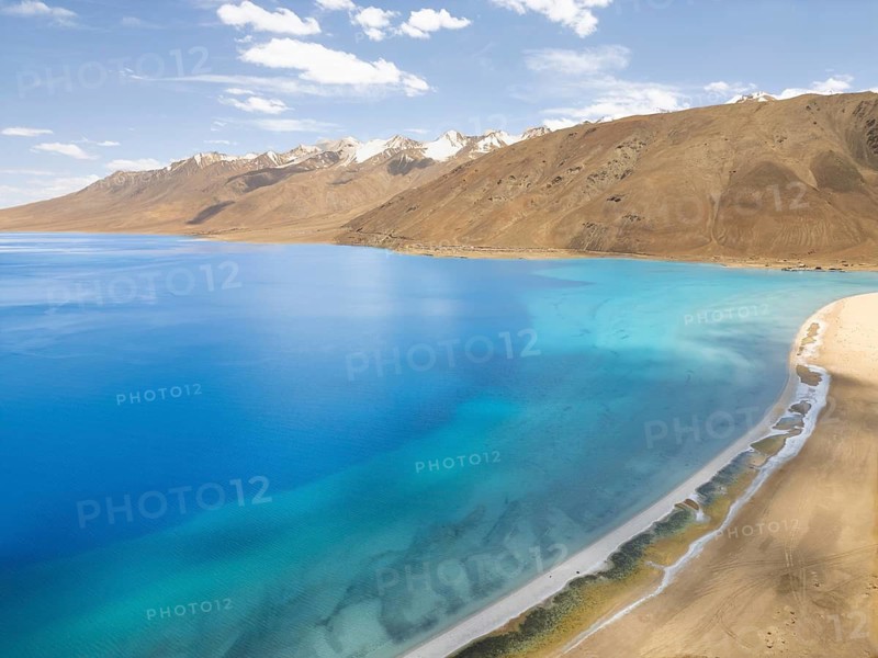 Breathtaking view of the serene Pangong Tso lake in Ladakh, India. The azure waters contrast with the stark, barren mountains under a clear blue sky, creating a tranquil landscape