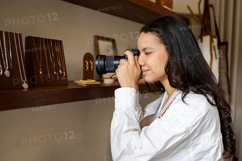 A photographer takes close up shots of displayed jewelry in a bag store. The focus is on capturing intricate details of the elegant necklaces and earrings on wooden stands