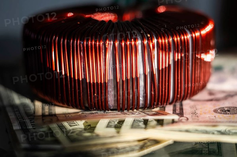 Industrial copper wire coil placed near US dollar bills, symbolizing the link between technology, manufacturing costs, and financial energy investments in Poland