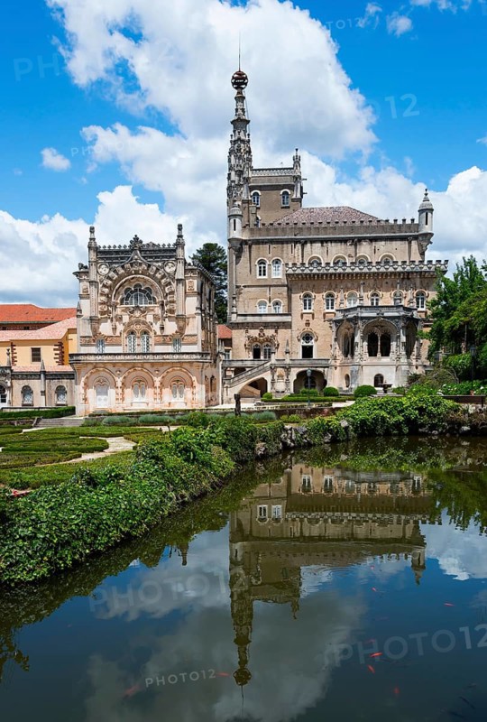 Ein prächtiges Schloss mit reich verzierter Fassade, umgeben von üppiger Vegetation und einem ruhigen Fluss, der das Gebäude reflektiert, Palácio Hotel do Buçaco, Mata Nacional do Buçaco, National-Wald von Bussaco, Bucaco, Mealhada, Beira Litoral, Portugal