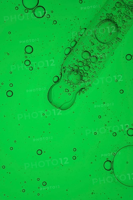 A close up macro shot of aloe vera oil for serum cosmetic, forming a vibrant abstract pattern. The translucent droplets float against a bright background, creating a mesmerizing visual