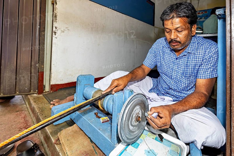 A concentrated man sits at a grinding machine and works on an object, The gemstone cutters in the city of Ratnapura in Sri Lanka