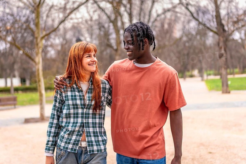 Young multiracial couple walking together in a park, chatting and smiling while enjoying each other's company in a vibrant spring setting