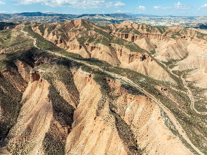 Winding gravel road on a plateau, surrounded by colorful canyons and gorges, aerial view, Gorafe Desert, UNESCO Granada Geopark, Granada province, Andalusia, Spain