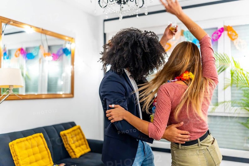 Diverse and multi-ethnic friends dancing embracing from the back together latin music during home party