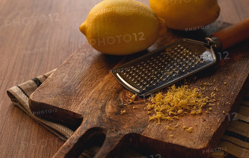 Lemons and grated orange peel, with a zest grater, on a chopping board, close-up, no people