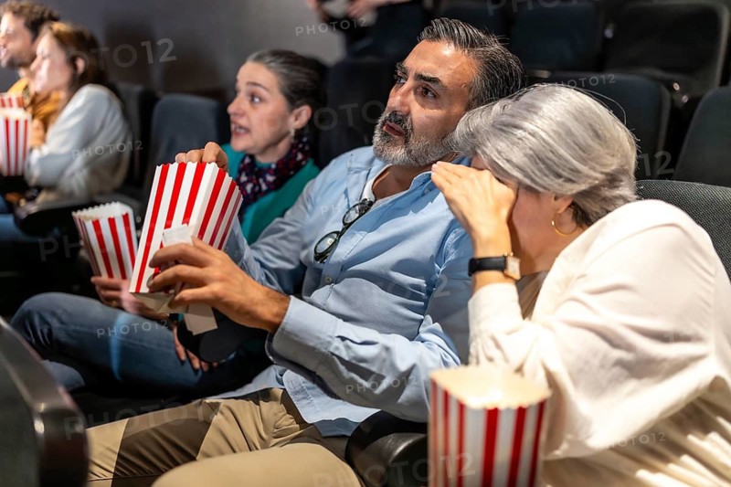 Group of friends and family enjoying a movie at the cinema, eating popcorn and showing a wide range of emotions