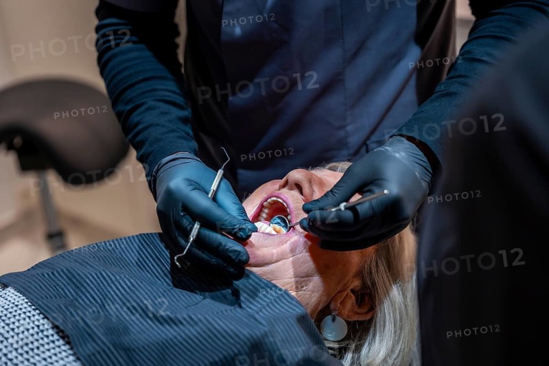 Dentist wearing black gloves examining teeth of a senior woman lying in dentist chair during a check up