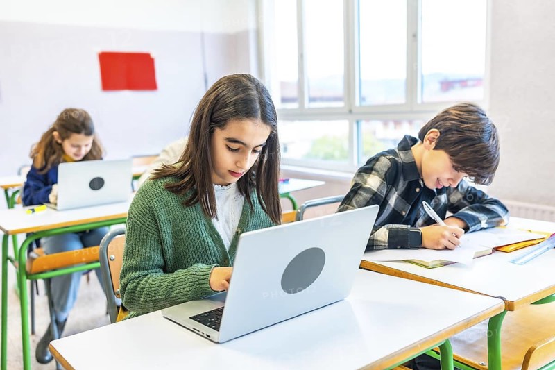 Elementary school students engaging in classroom activities, using laptops for research and diligently taking notes during lessons