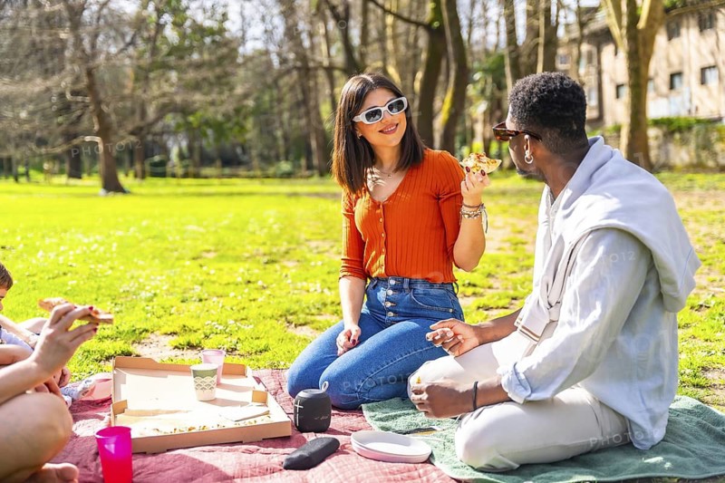 Young people enjoying a sunny day picnic in a city park, sharing delicious pizza and laughter while relaxing on the grass together