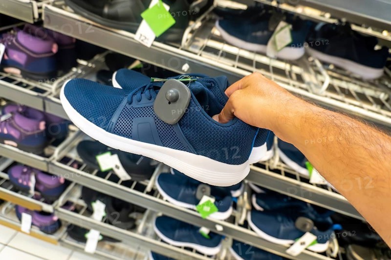 A person is holding a blue shoe with a tag on it. The shoe is on display in a store