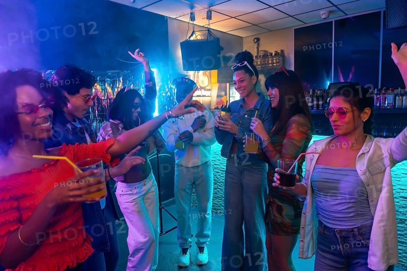 Young diverse friends enjoying music, drinks, and lively conversation in a vibrant nightclub, celebrating together under colorful neon lights with an energetic atmosphere