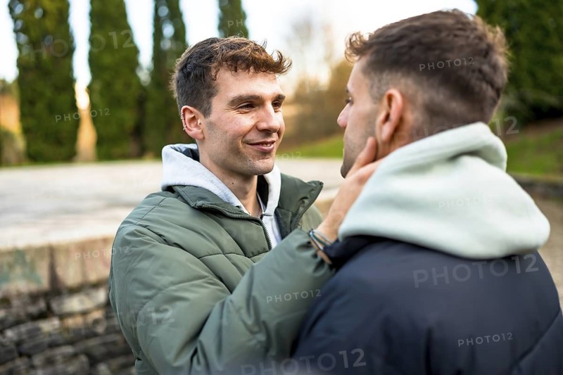 Two men embracing and smiling at each other, sharing a tender moment filled with love and intimacy in a beautiful outdoor park setting