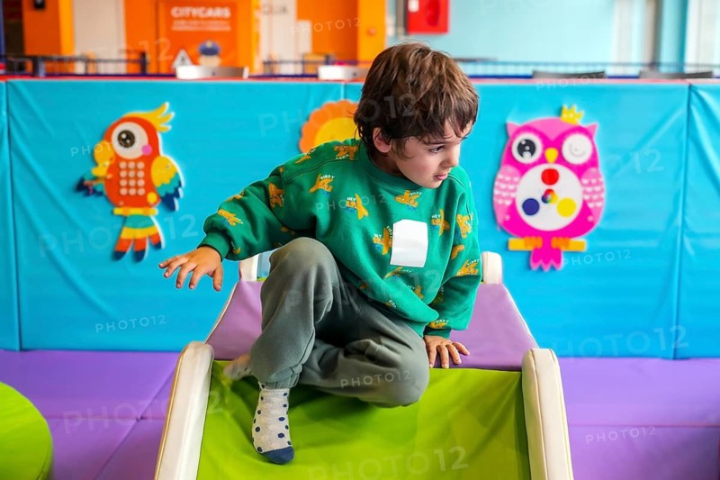 Young boy having fun crawling on a soft slide in a colorful indoor playground, enjoying his playtime